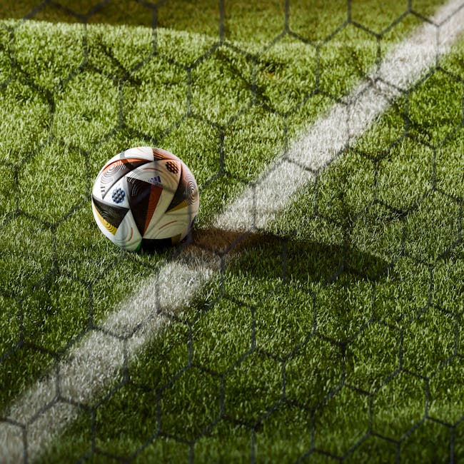 Soccer ball on a lush green field seen through netting, perfect for sports themes.